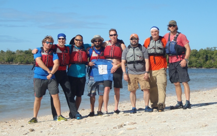 a group of people stand on a beach smiling while posing with a blue peter flag